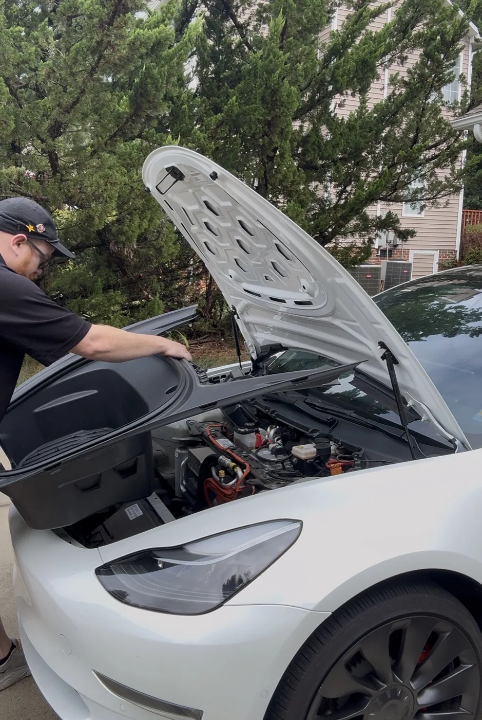 Aaron working beneath the open hood of a white Tesla at a residential location