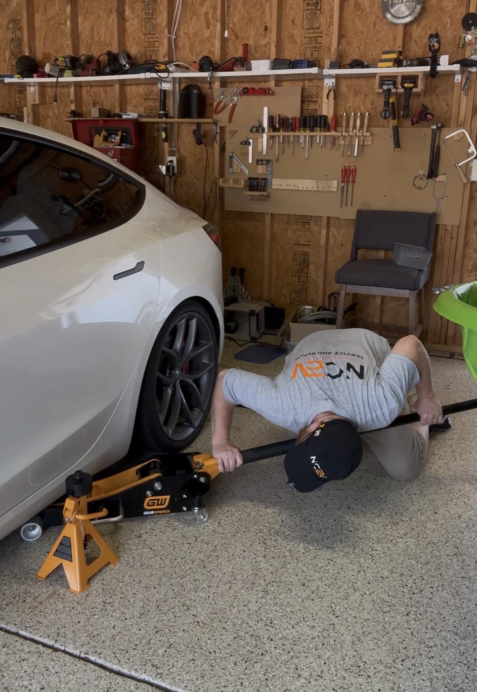 Aaron using a floor jack beside a white Tesla in a garage